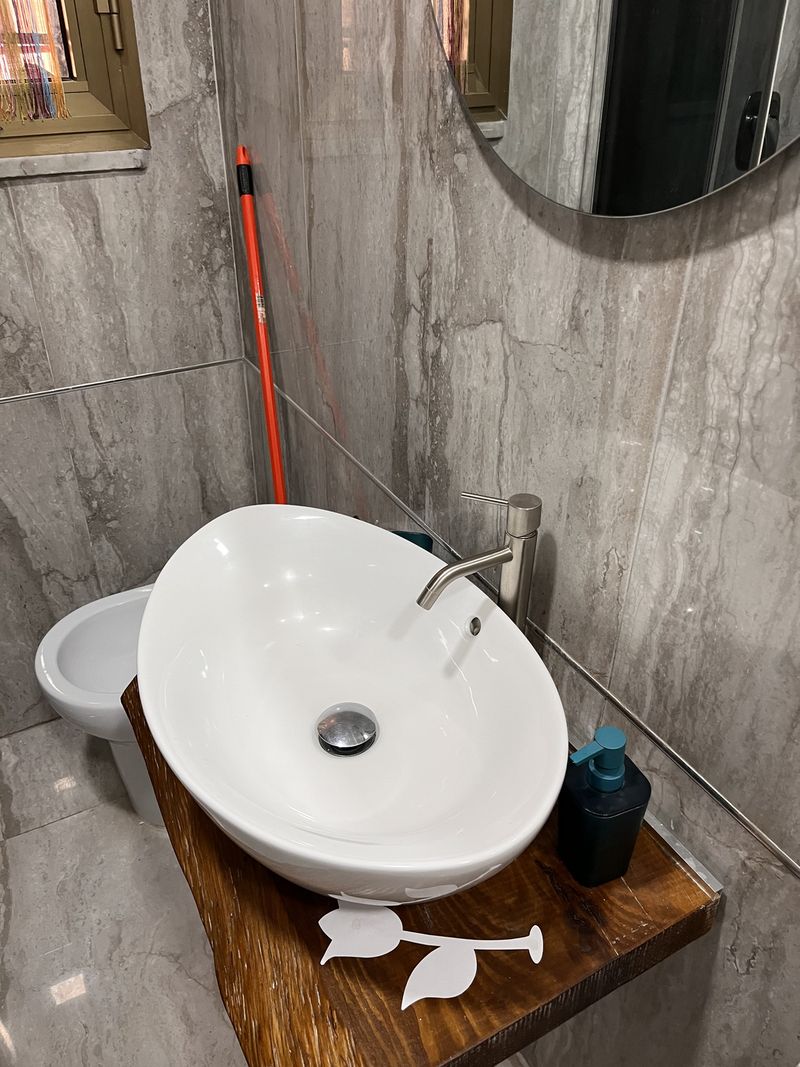 A round basin on a wooden shelf, set against the new marble-effect tiles.