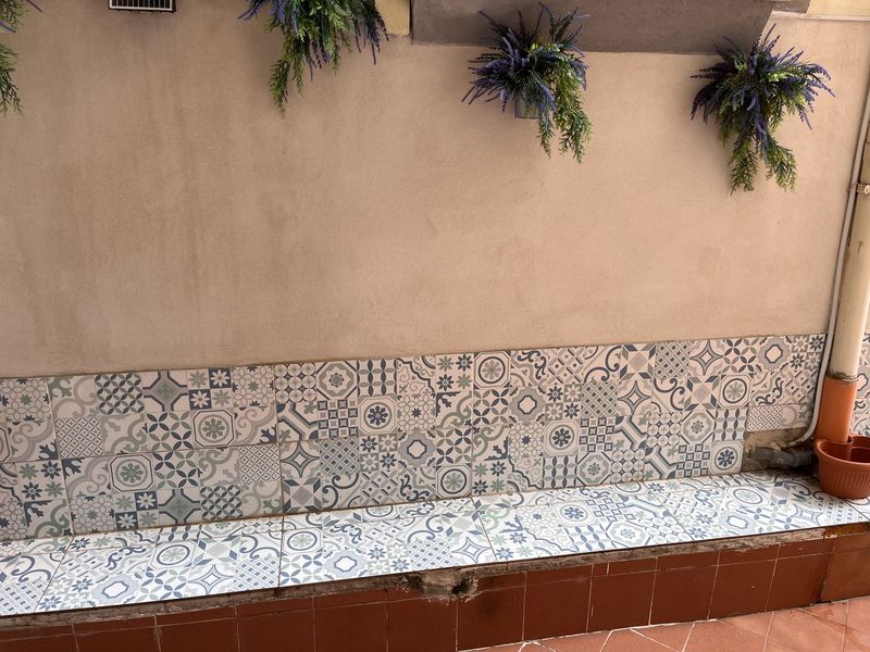 A long bench clad in blue-and-white tiles, beneath the hanging plants.