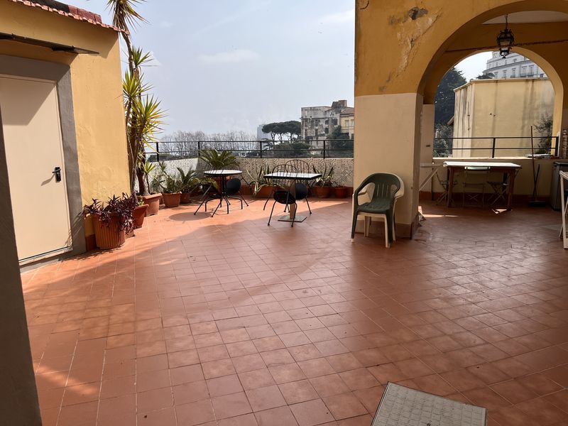 The spacious terrace, with little tables, palms in pots and an arch in the yellow facade.