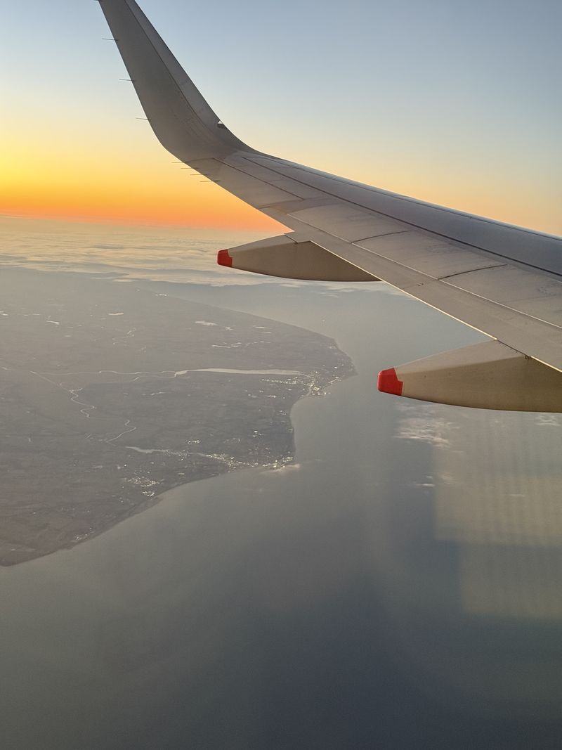 Dal finestrino dell'aereo l'orizzonte si tinge di arancione, con la costa molto più in basso.
