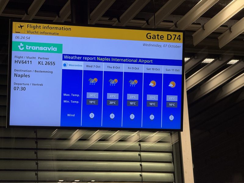 Waiting at gate D74, with the Naples weather already on the screen.