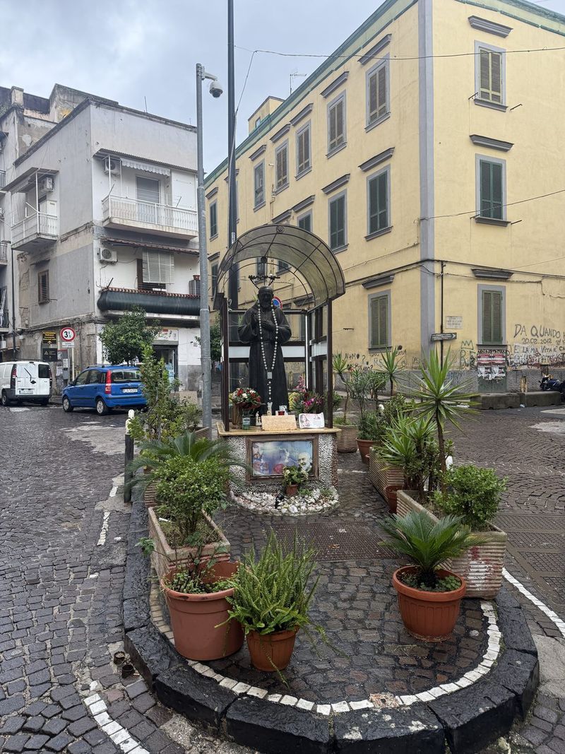 A statue of Padre Pio with plants, right in the middle of the street.